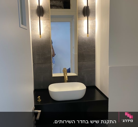 קיר שיש כהה עם כיור לבן וברז זהב
